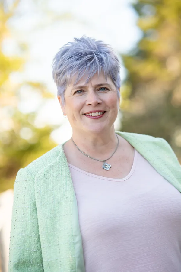 Trish McCourt is outside in a light green blazer, smiles and looks toward the camera. Photo credit: Adam Bissonette