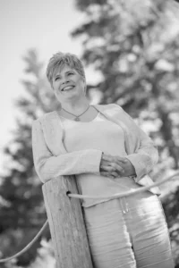 Trish McCourt outside, leaning on a fencepost, looking at the scenery.